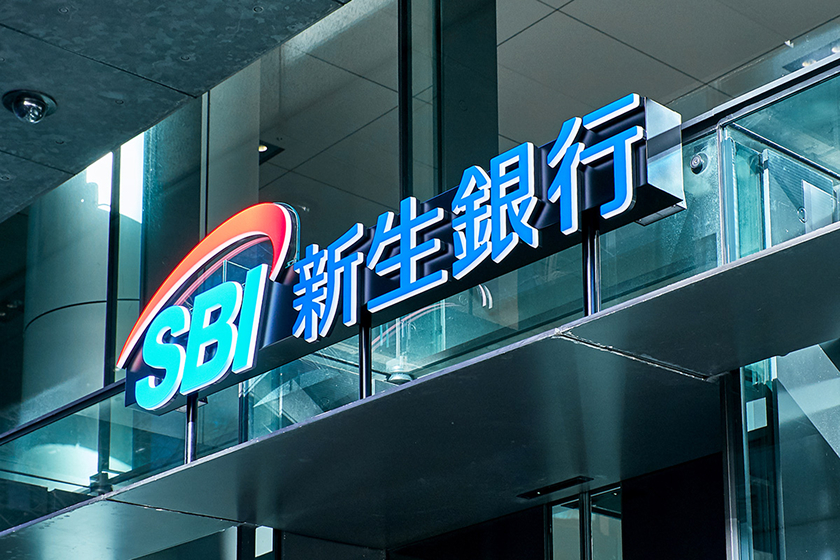ビルの入り口に設置された、青い文字で光る立体的な「SBI新生銀行」のブランドロゴサイン看板